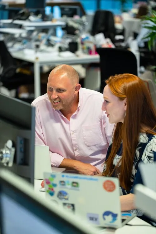 Colleagues discussing work while enjoying the Brinkee platform at their desk